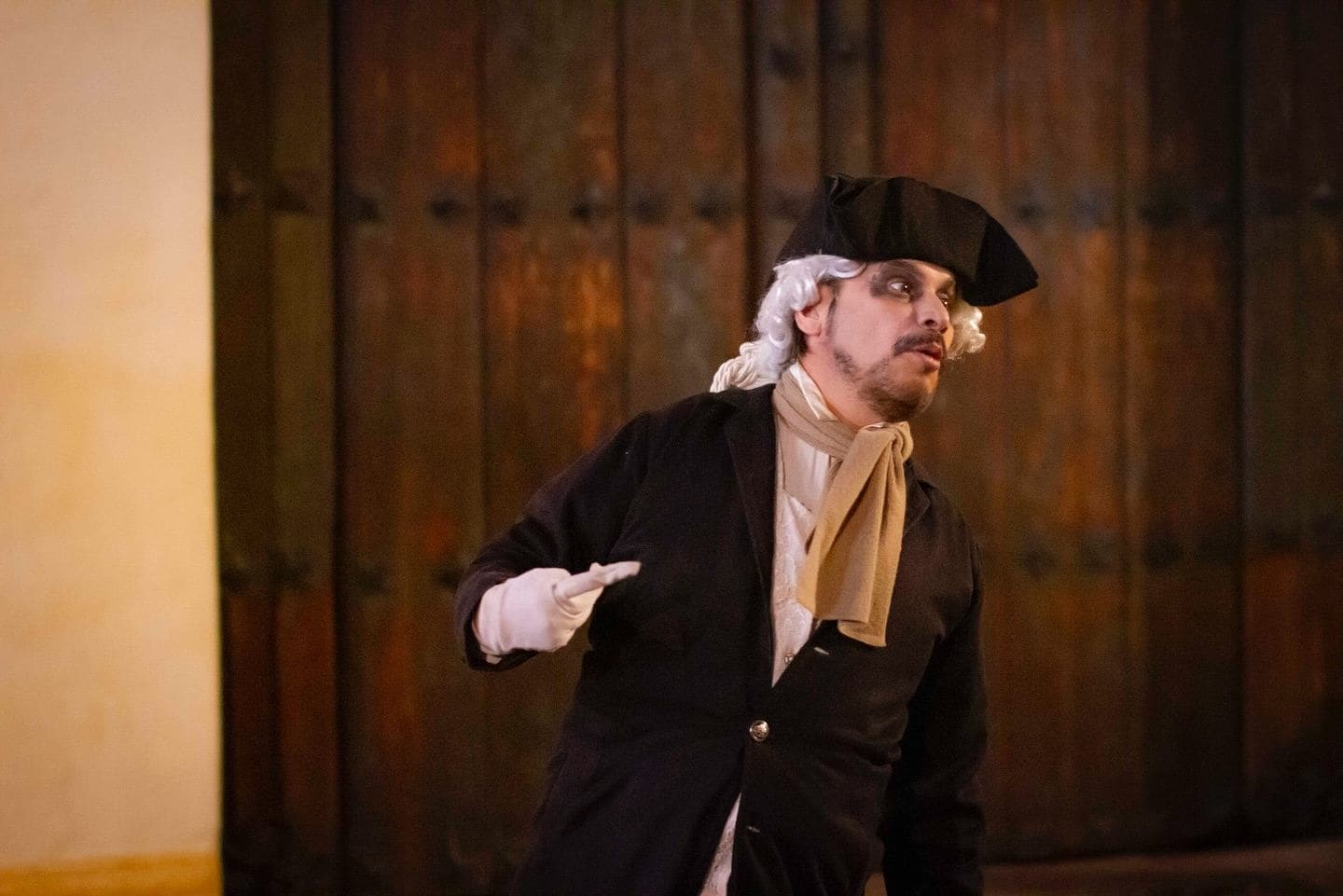 Actor caracterizado con tricornio y peluca blanca frente a una puerta colonial