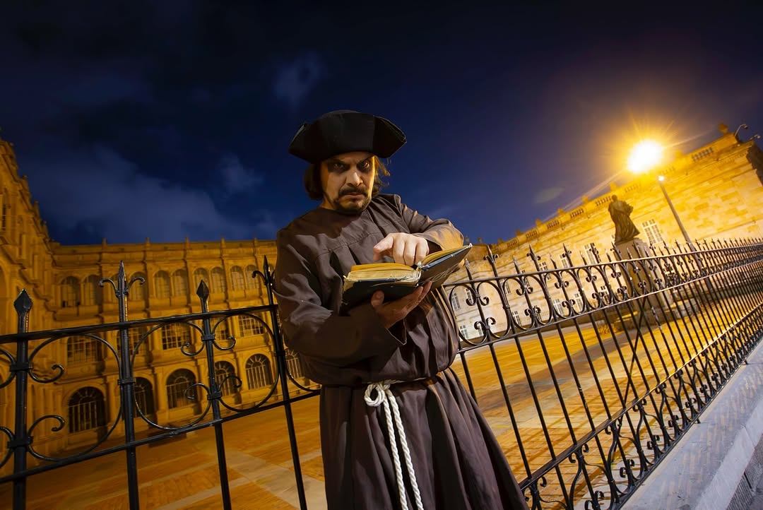 Actor vestido de monje con un libro en la Plaza de Bolívar de noche